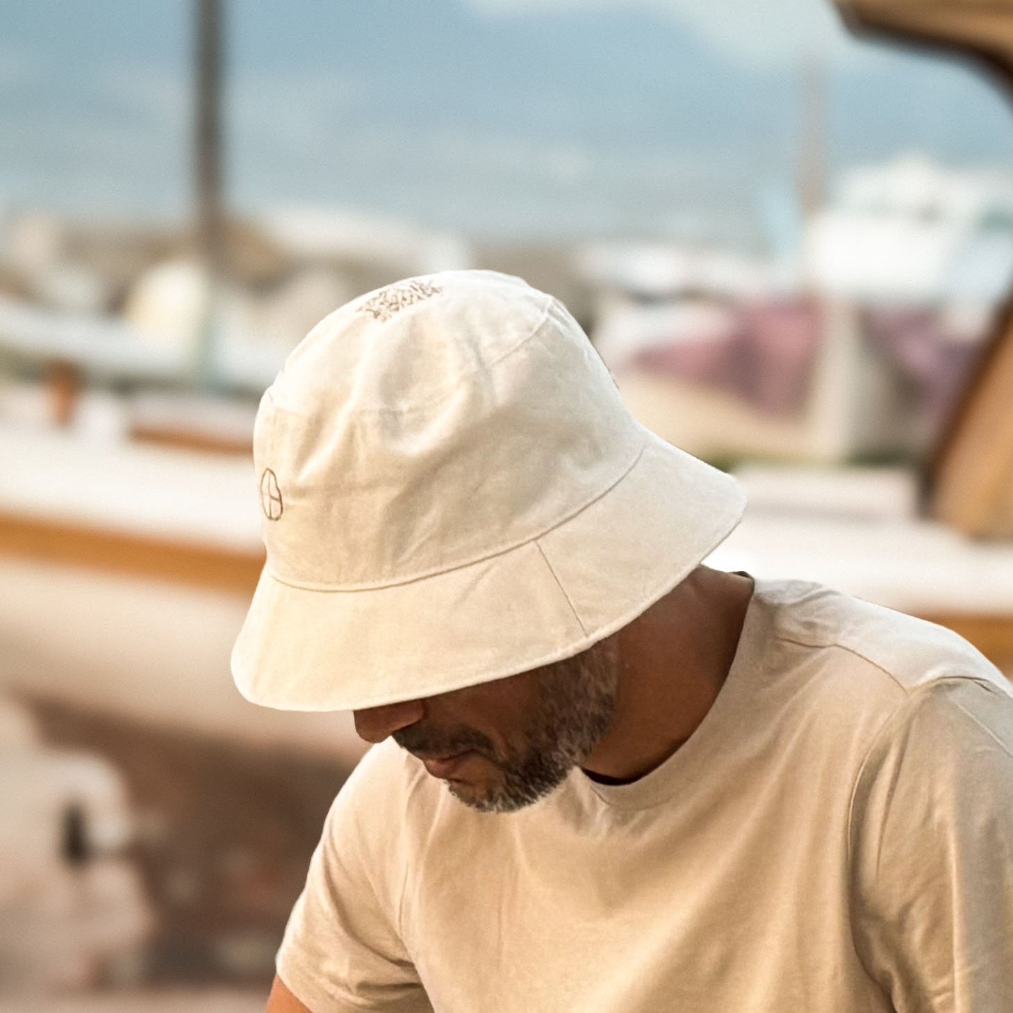 Minimalist bucket hat with CARDHEIR logo, worn by man at the seaside – natural cotton design