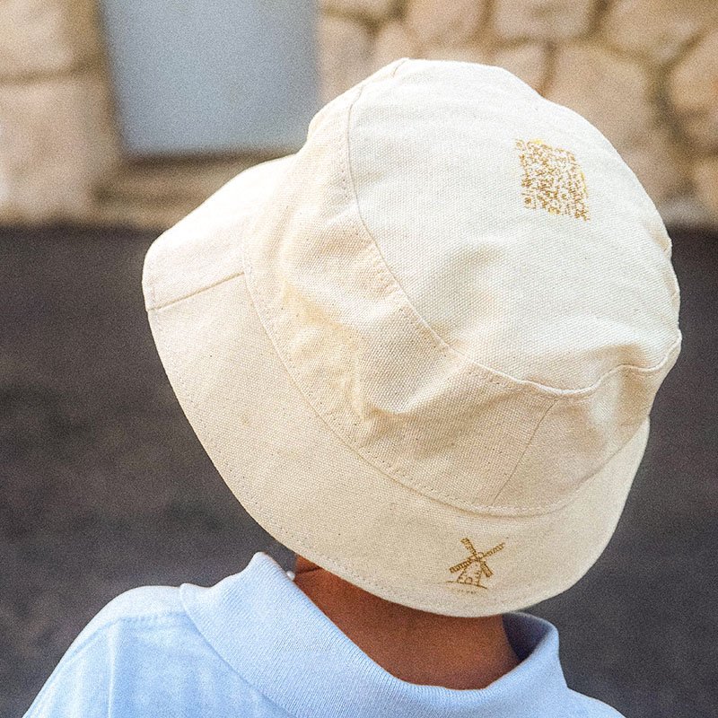 Kalani wearing a natural cotton CARDHEIR® bucket hat with gold-printed windmill and QR code, symbolizing Amsterdam heritage and sustainable design.