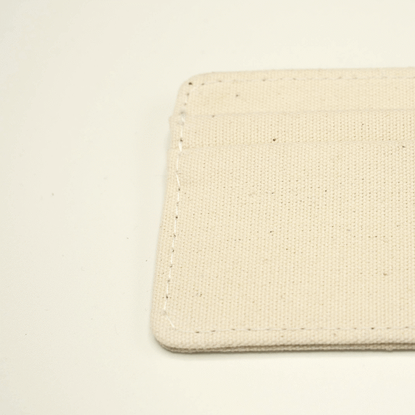 Close-up of the top-left corner of a natural cotton cardholder, showing detailed stitching and undyed fabric texture.