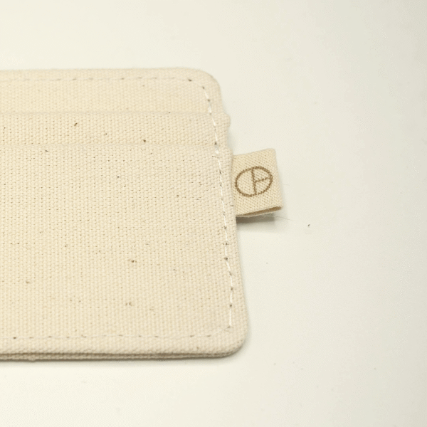 Close-up of a natural cotton cardholder showing detailed stitching and a small tab with the CARDHΞ↓R logo.