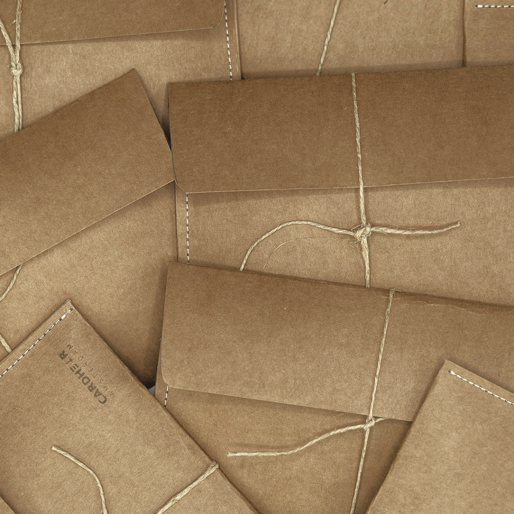 Handmade kraft paper envelopes with natural twine ties, used for packaging CARDHΞ↓R Raw Collection products, laid out in a flat lay.