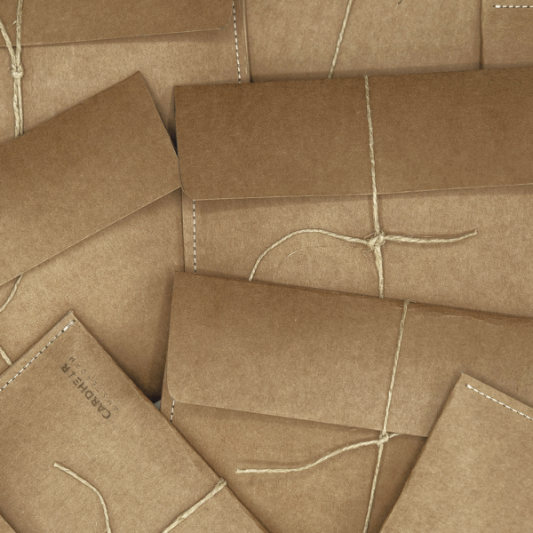 Handmade kraft paper envelopes with natural twine ties, used for packaging CARDHΞ↓R Raw Collection products, laid out in a flat lay.
